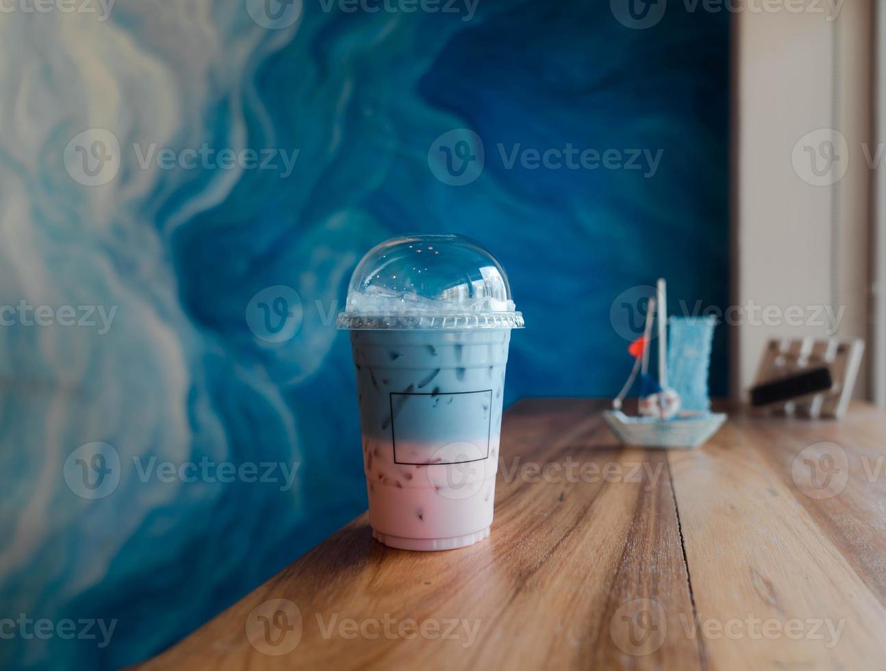 ice strawberry milk mixed with butterfly pea milk in gradient on wooden table, cool refreshing beverage. takeaway cup. photo