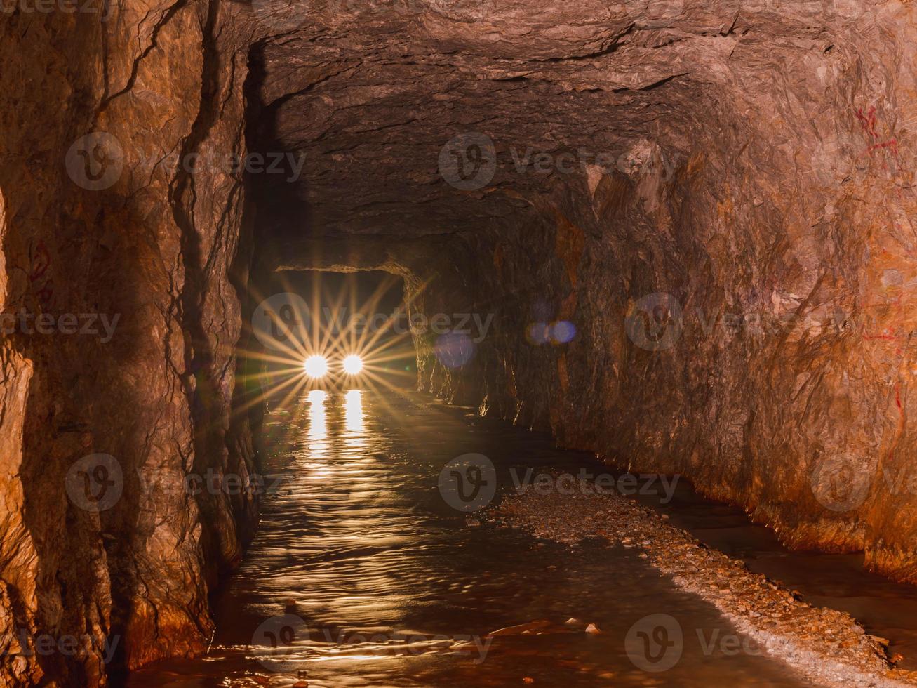 car lights from inside deep old mining tunnel cave with reflection. rock wall cave with water lodge rocky road. adventure travel in Thong Pha Phum, Kanchanaburi, Thailand called 3D tunnel. photo