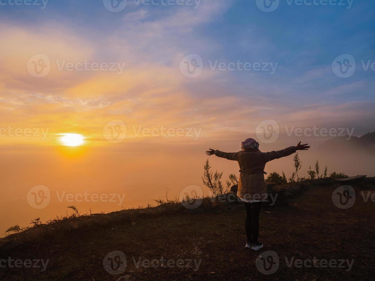 Asian woman with freedom arms open standing on mountain peak at Pha Tang view point 104 with river view and sea mist and sun rise in fog sky. travel place in Chaing Rai, Thailand photo