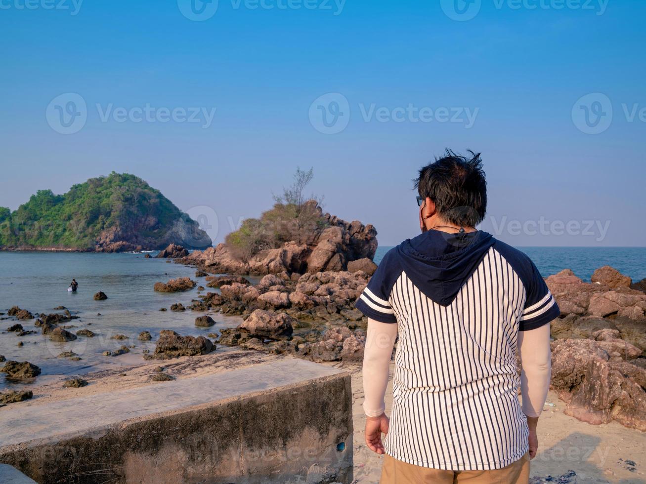 hombre en la parte de atrás de pie y mirando la vista de la isla desde la costa foto