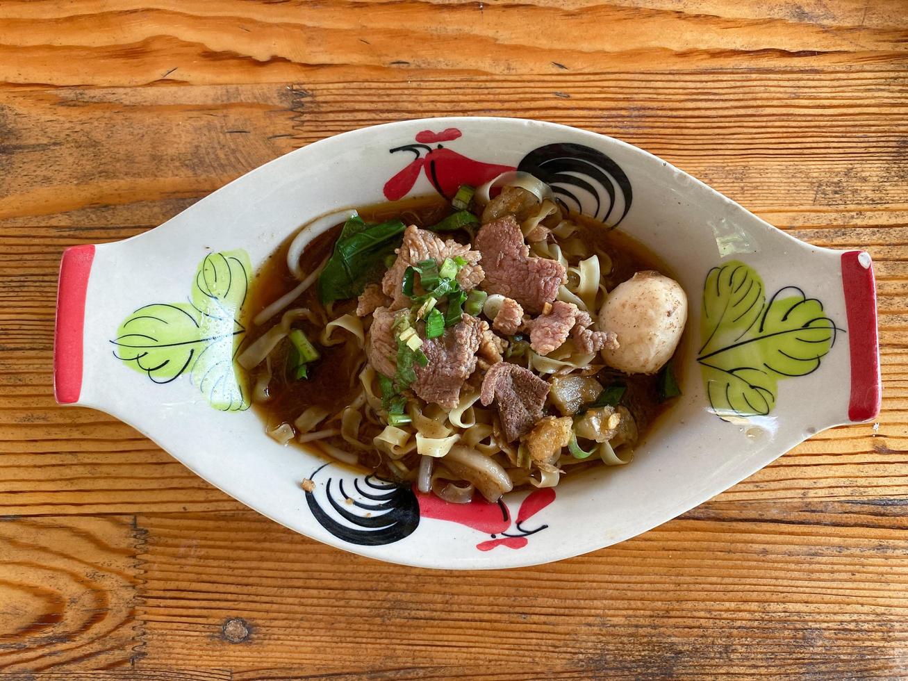 Pork noodles in a bowl that is on a wooden table. photo