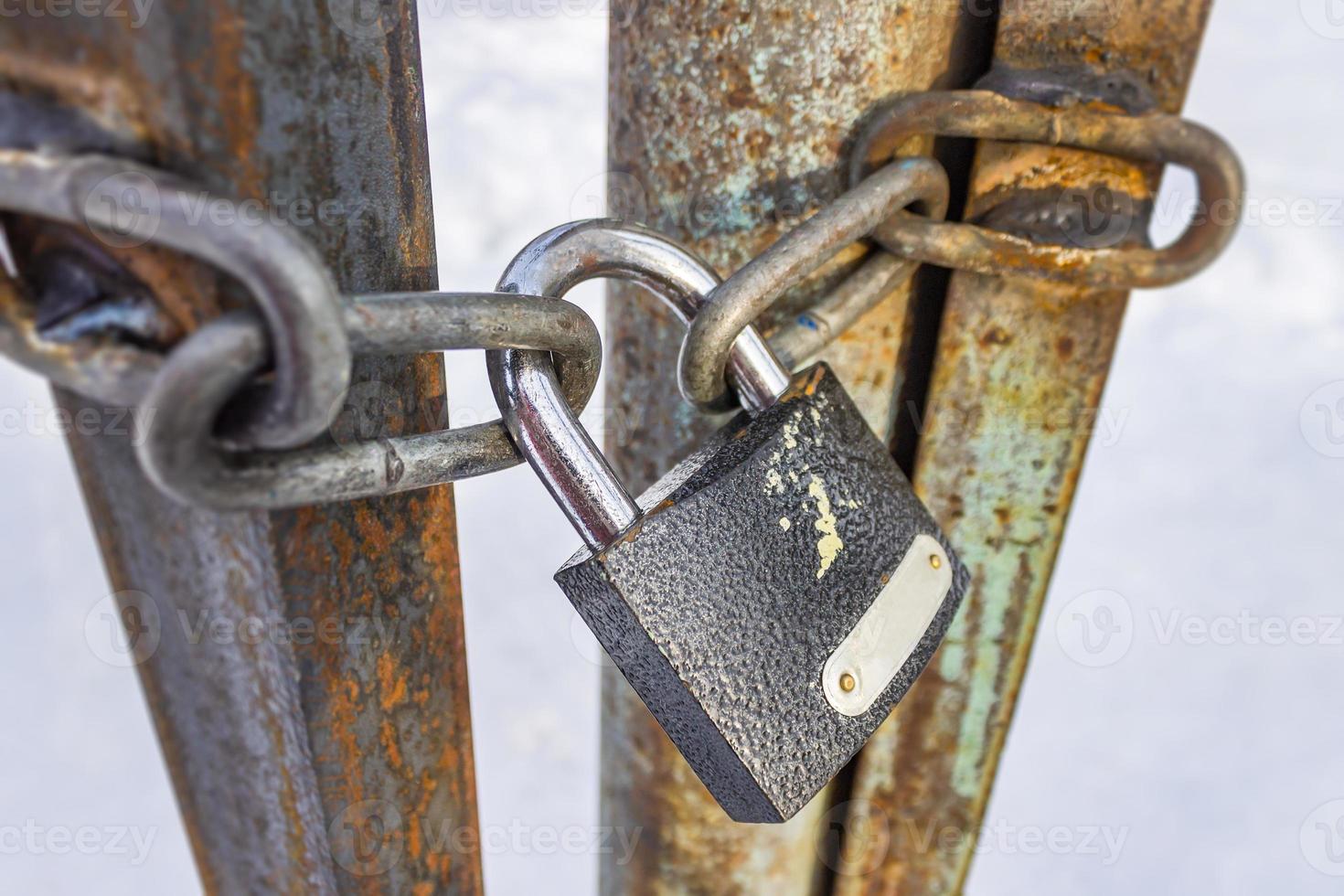 Closed padlock and chains hanging on old and rusty iron gates photo