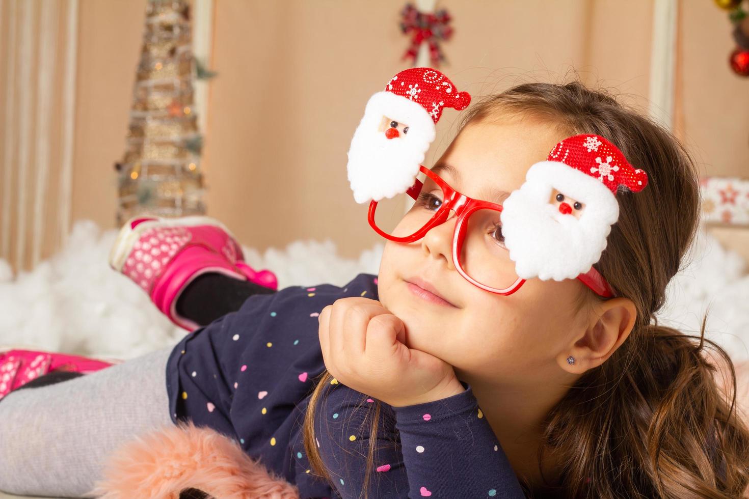 Little girl wearing santa glasses and making faces photo