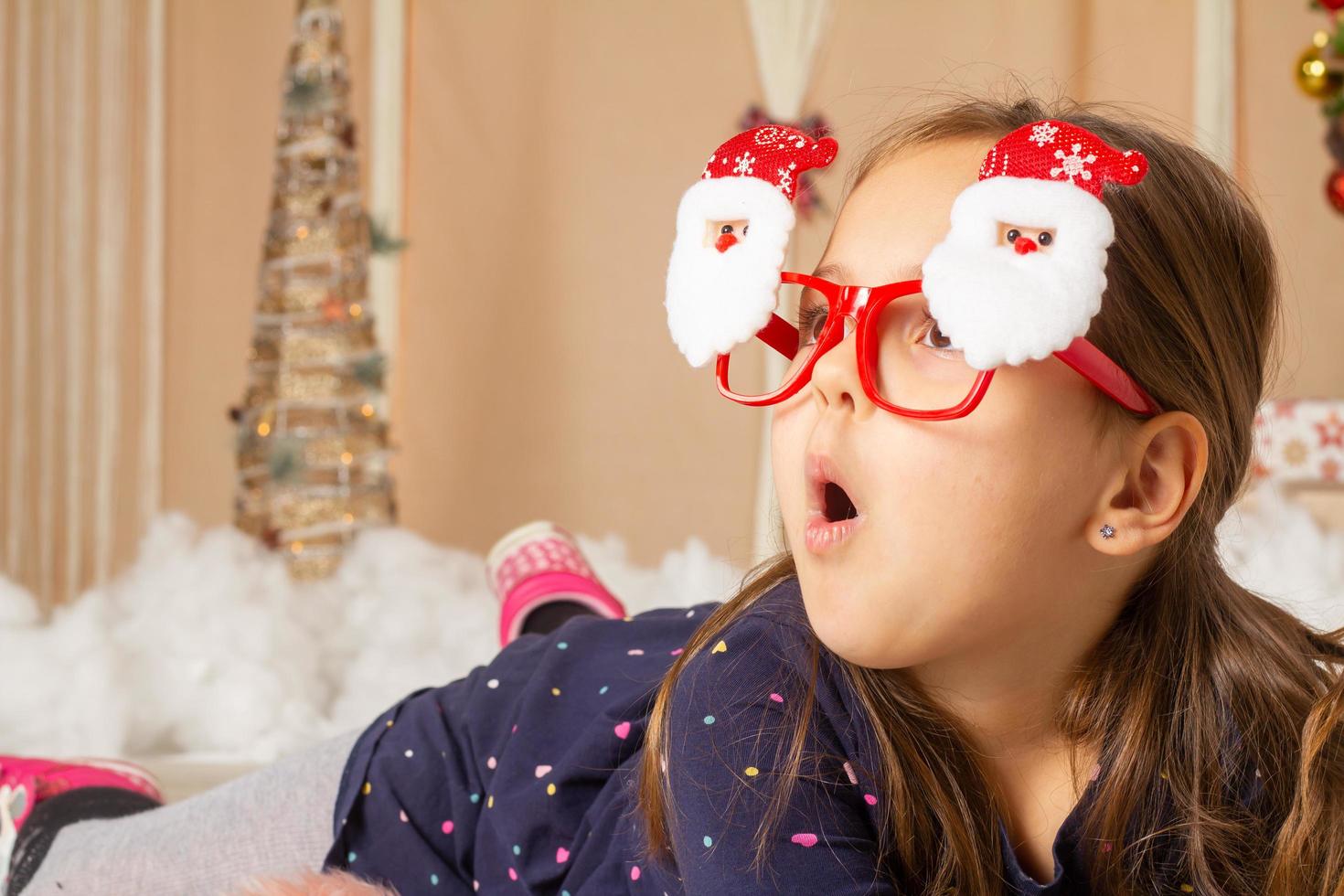 Little girl wearing santa glasses and making faces photo