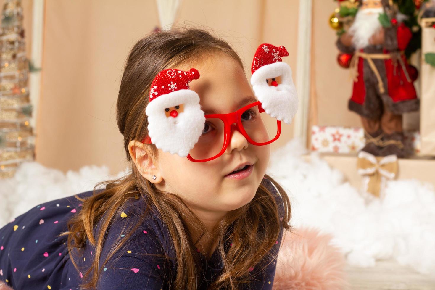 Little girl wearing santa glasses and making faces photo