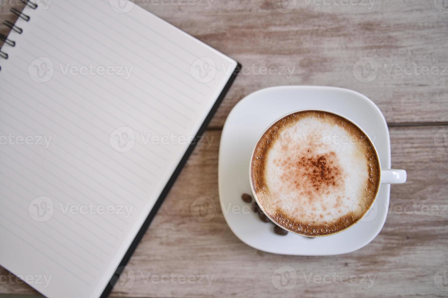 abra un cuaderno blanco en blanco, un bolígrafo y una taza de café en el escritorio foto