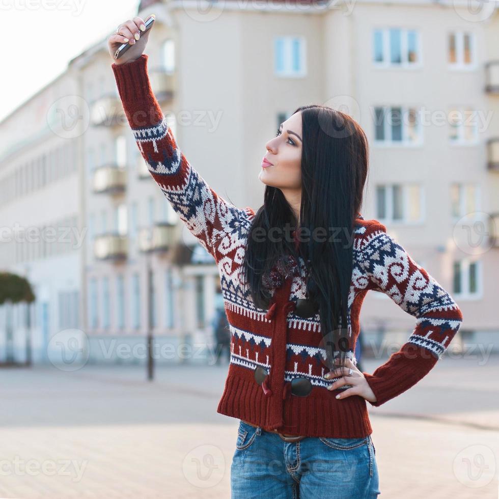 Beautiful girl doing Selfie on phone in city. photo