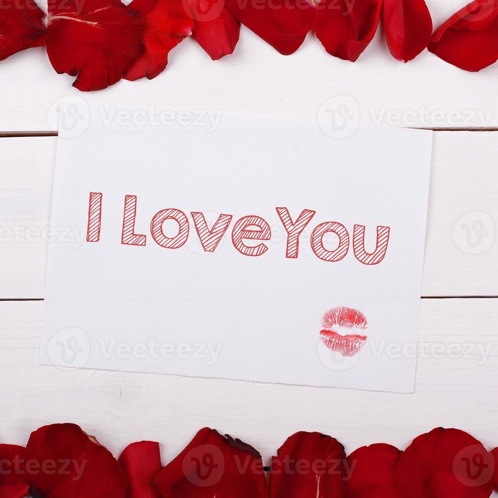 Sheet of paper for text I Love You with a kiss. Note and rose petals on the table photo