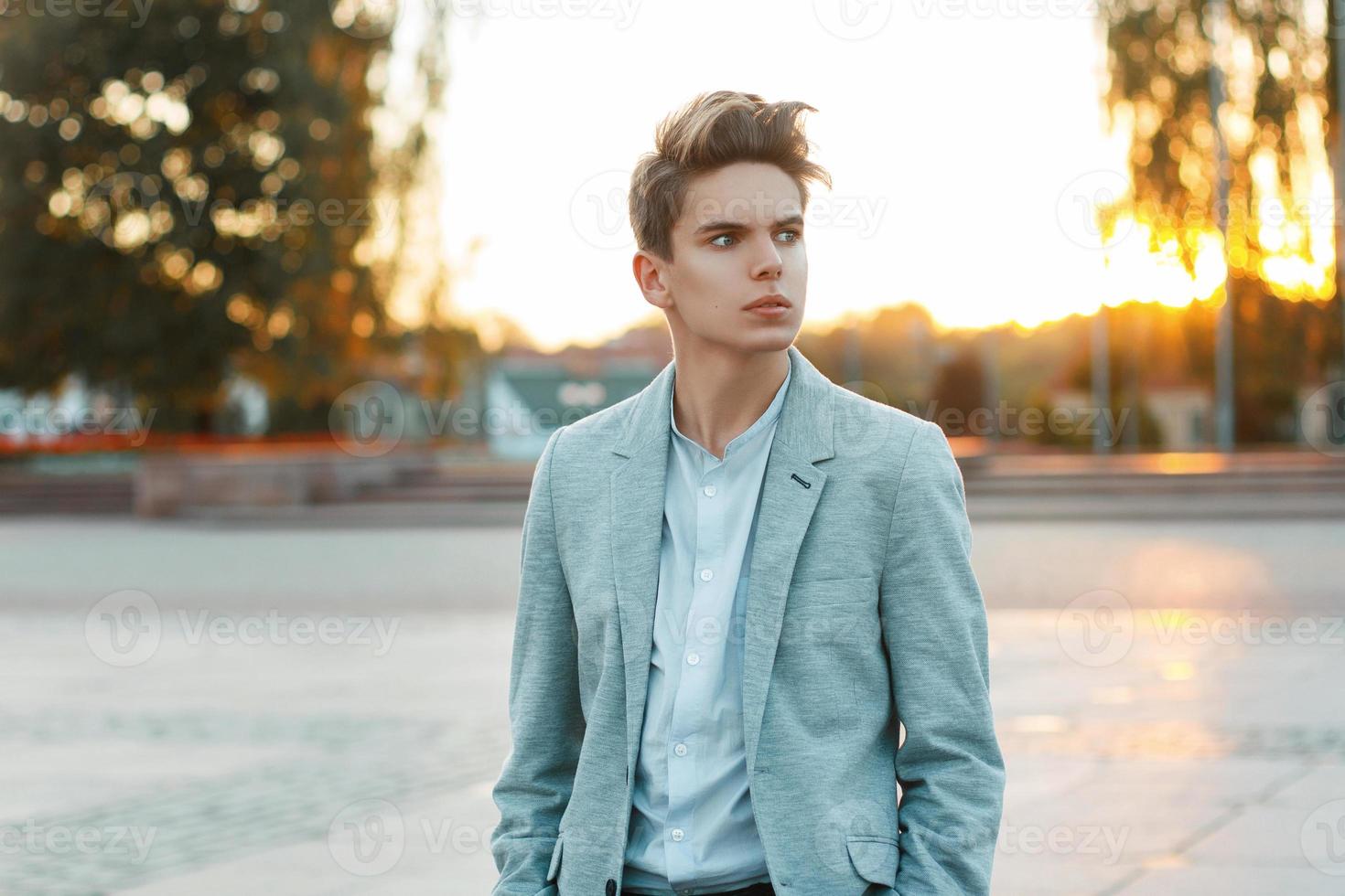 Handsome young businessman in a jacket and shirt outdoors at sunset photo