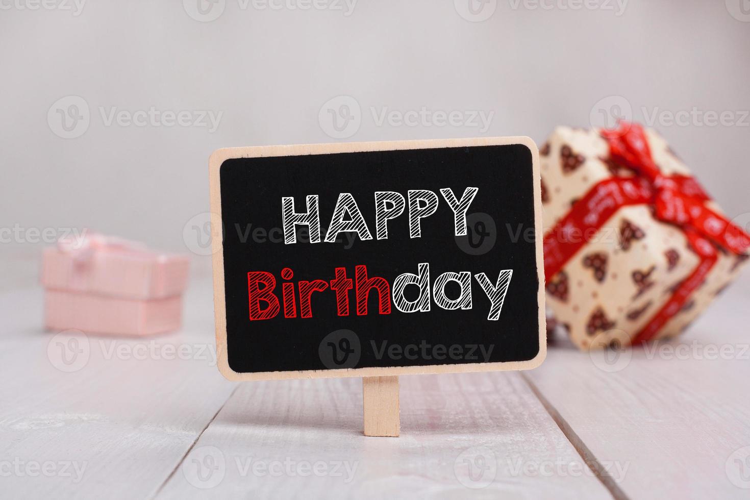 Black chalkboard with the Happy Birthday text on the table on the background with gifts. photo