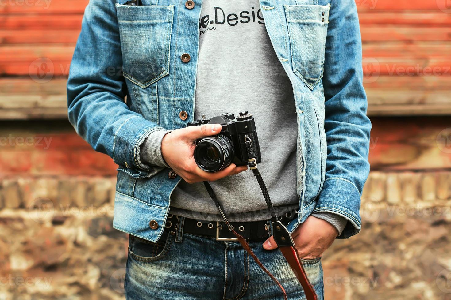 Fotógrafo hipster con estilo en ropa de mezclilla elegante sosteniendo una cámara foto