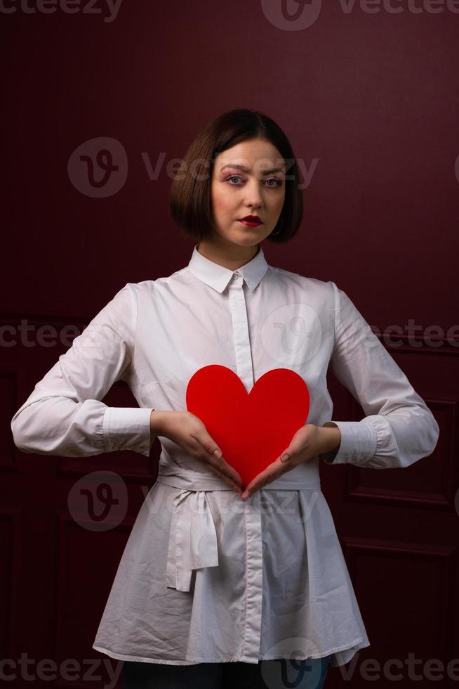 Short-haired woman with hands shaping a triangle holding heart shape in front of her photo