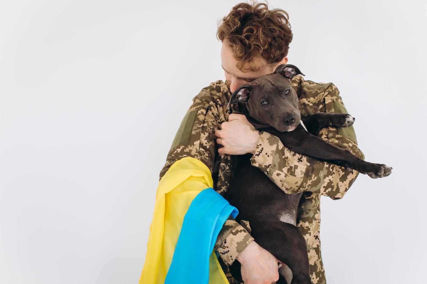 Ukrainian soldier in military uniform with a yellow and blue flag holds a dog in his arms on a white background photo