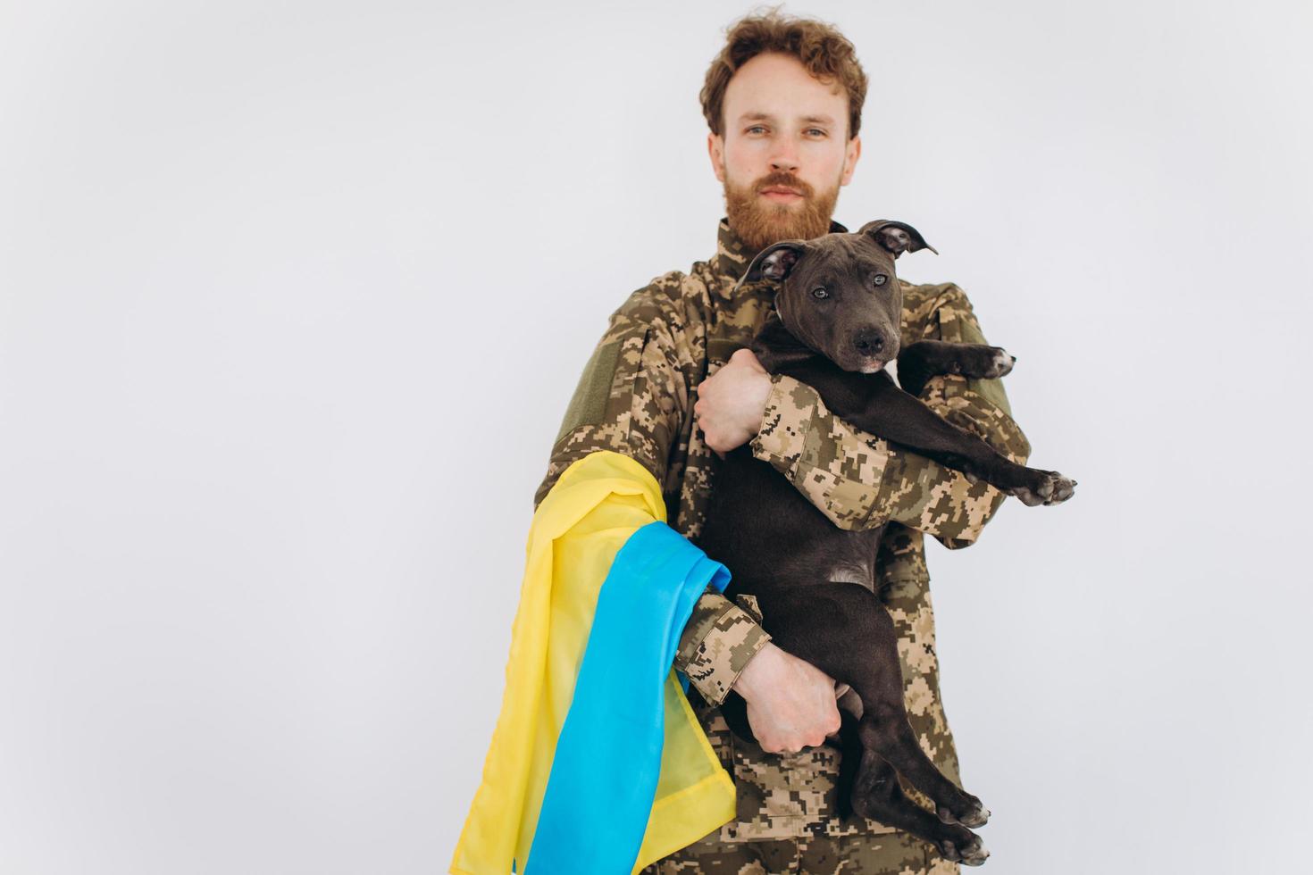 Ukrainian soldier in military uniform with a yellow and blue flag holds a dog in his arms on a white background photo