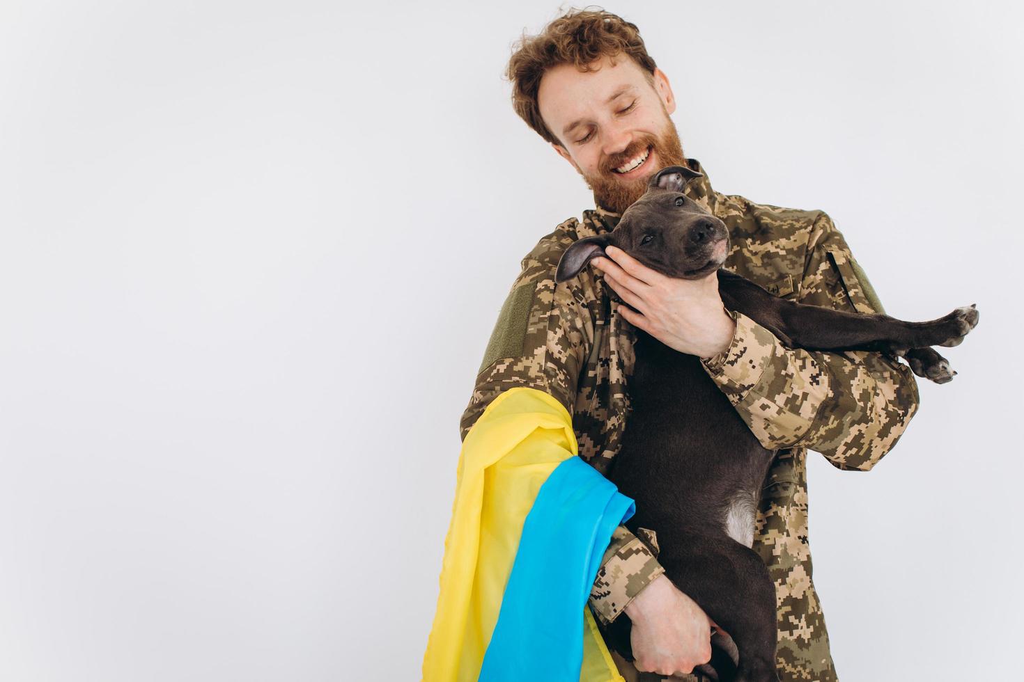 Ukrainian soldier in military uniform with a yellow and blue flag holds a dog in his arms on a white background photo