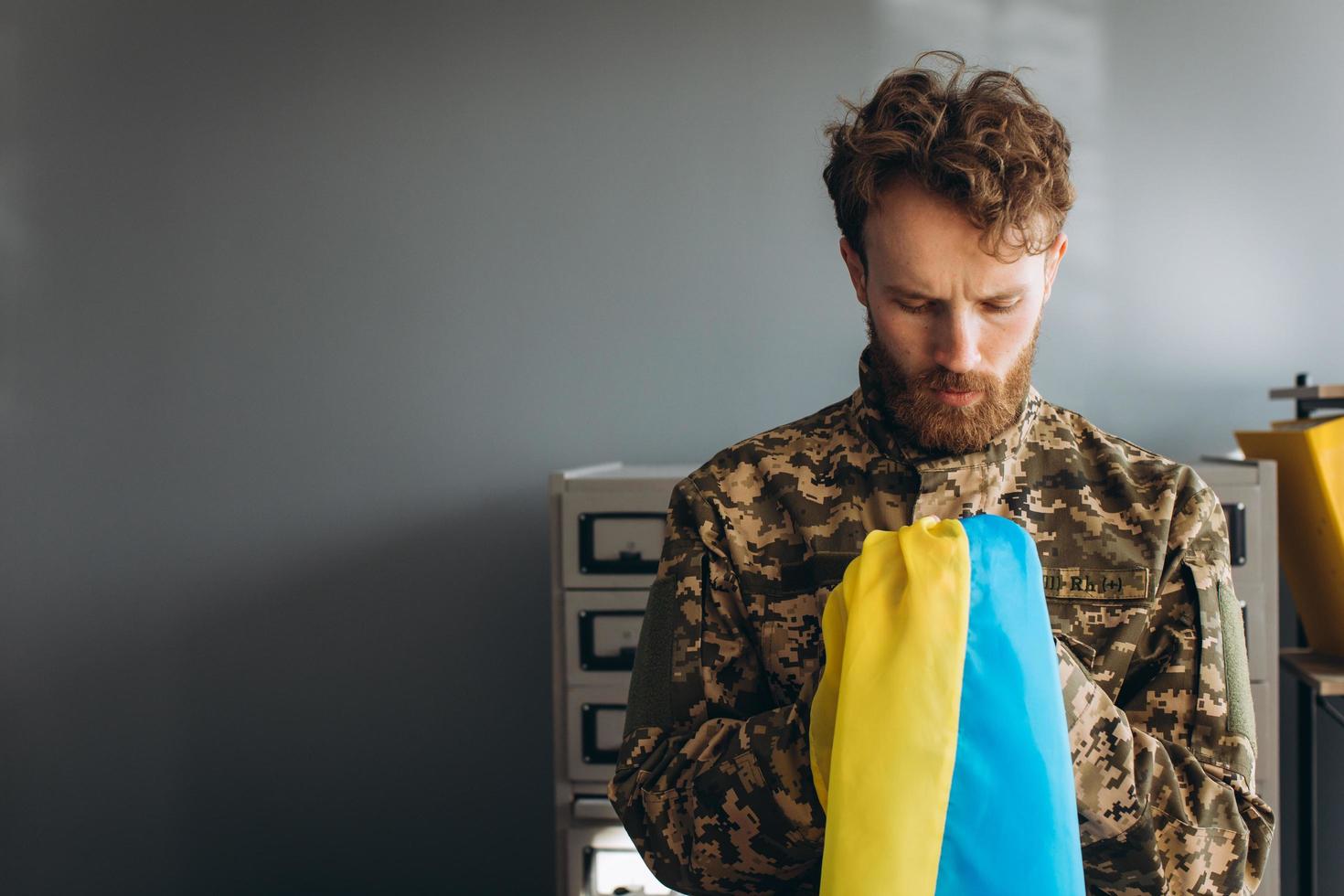 Ukrainian patriot soldier in military uniform holding a yellow and blue flag in the office photo