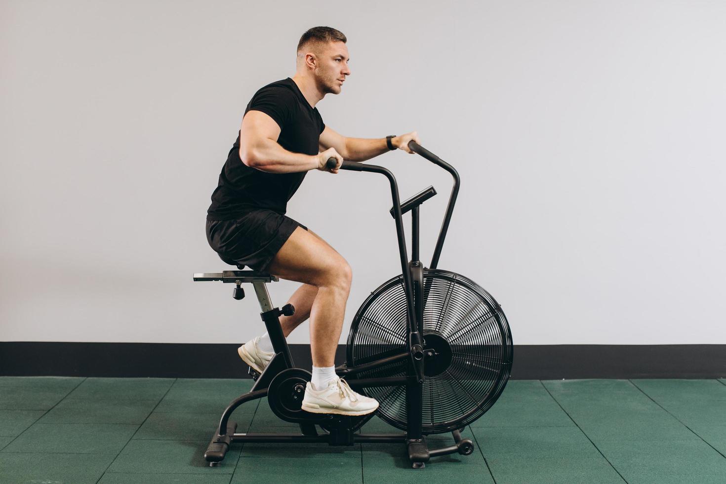 Strong man using air bike for cardio workout at cross training gym. photo