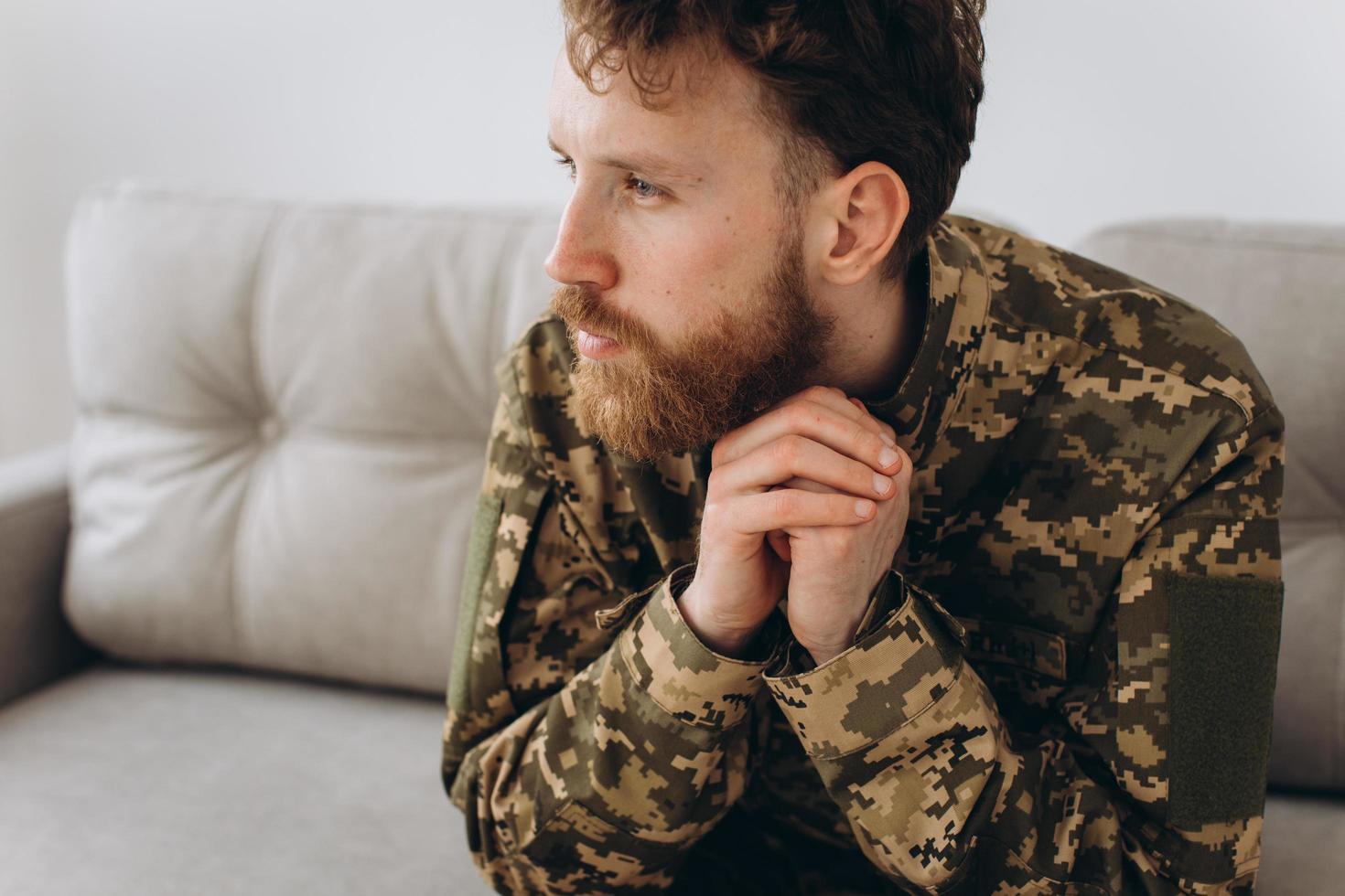 retrato de un emotivo joven soldado patriota ucraniano barbudo con uniforme militar sentado en el sofá de la oficina foto