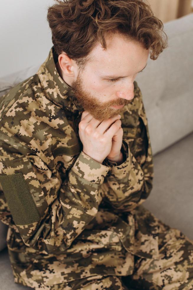 Portrait of emotional young bearded Ukrainian patriot soldier in military uniform sitting on the office sofa photo