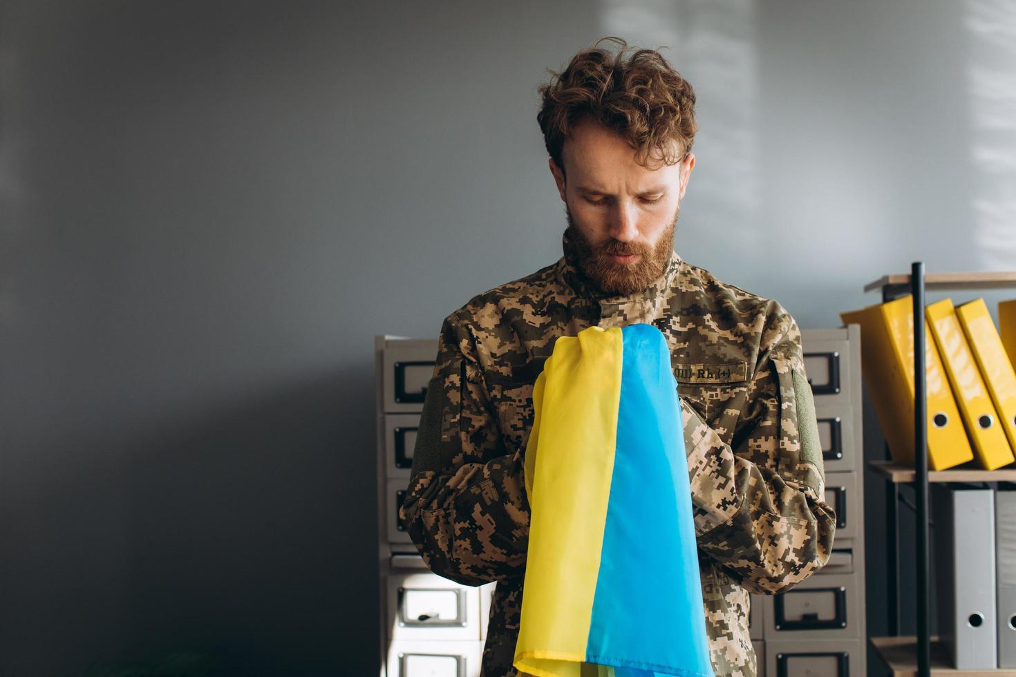 Ukrainian patriot soldier in military uniform holding a yellow and blue flag in the office photo