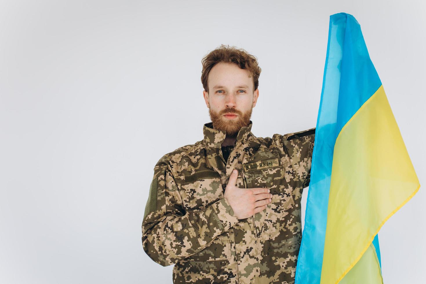 Ukrainian patriot soldier in military uniform holds a hand on a heart with a yellow and blue flag on a white background photo