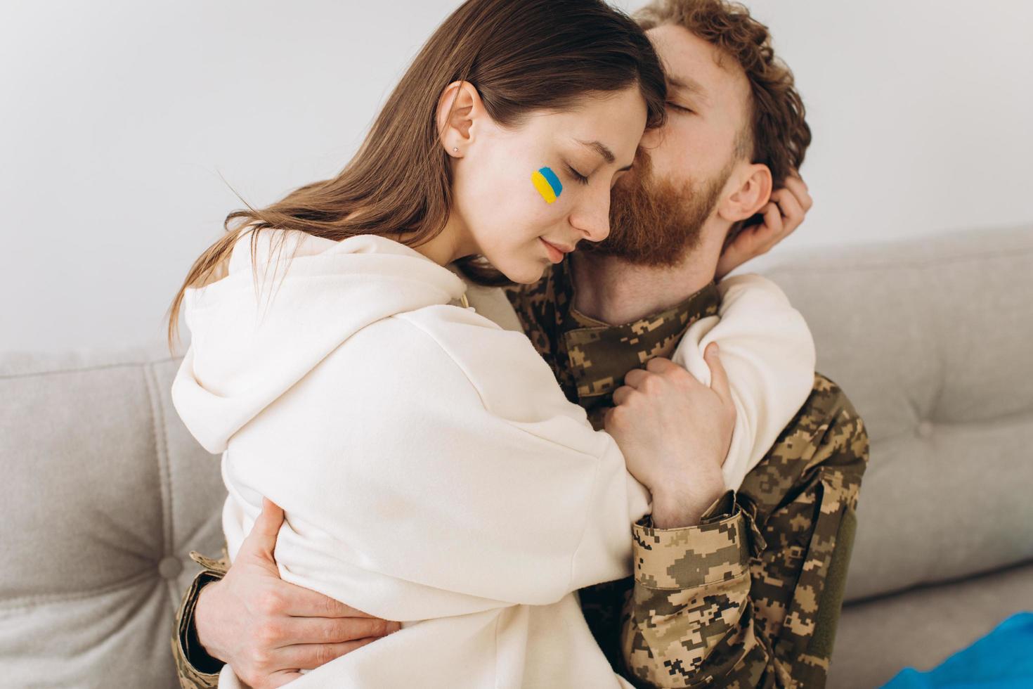 Ukrainian couple, military man in uniform kisses his girlfriend on the couch at home on a background of yellow and blue flag photo