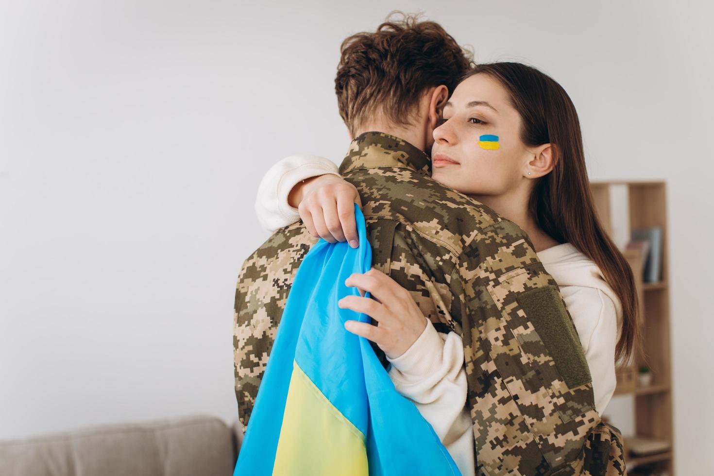 A Ukrainian girl hugs and holds a yellow and blue flag of a military man in uniform and says goodbye to him. photo
