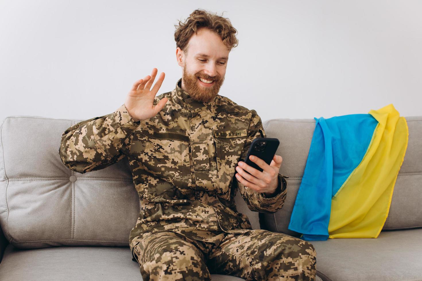 A Ukrainian soldier in military uniform is sitting on a sofa in the office and talking on the phone photo