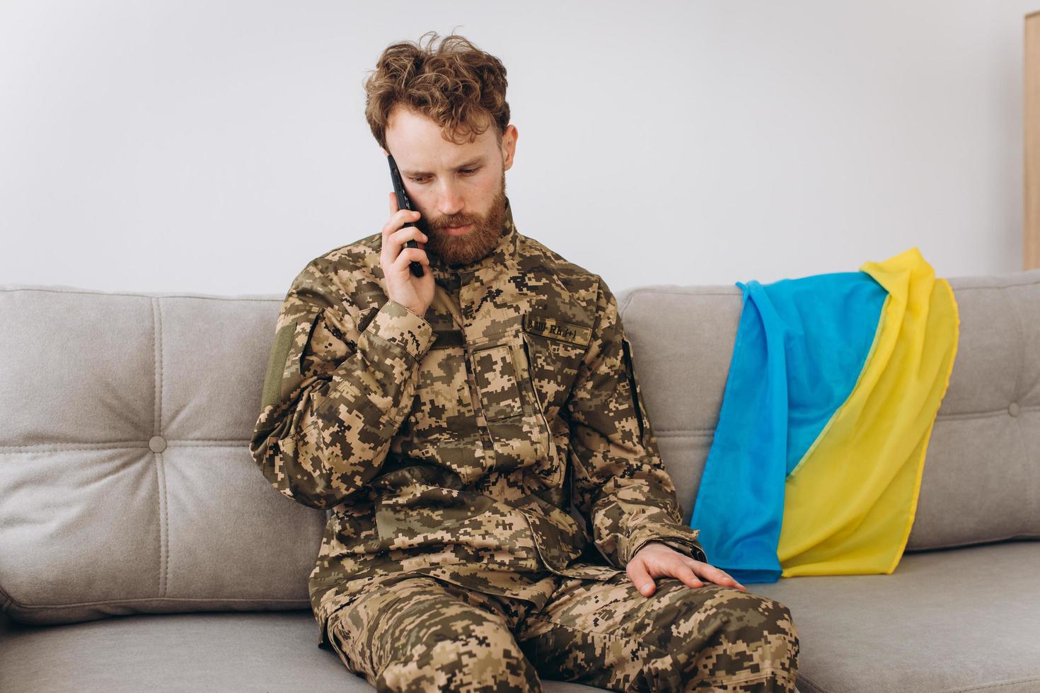 A Ukrainian soldier in military uniform is sitting on a sofa in the office and talking on the phone photo