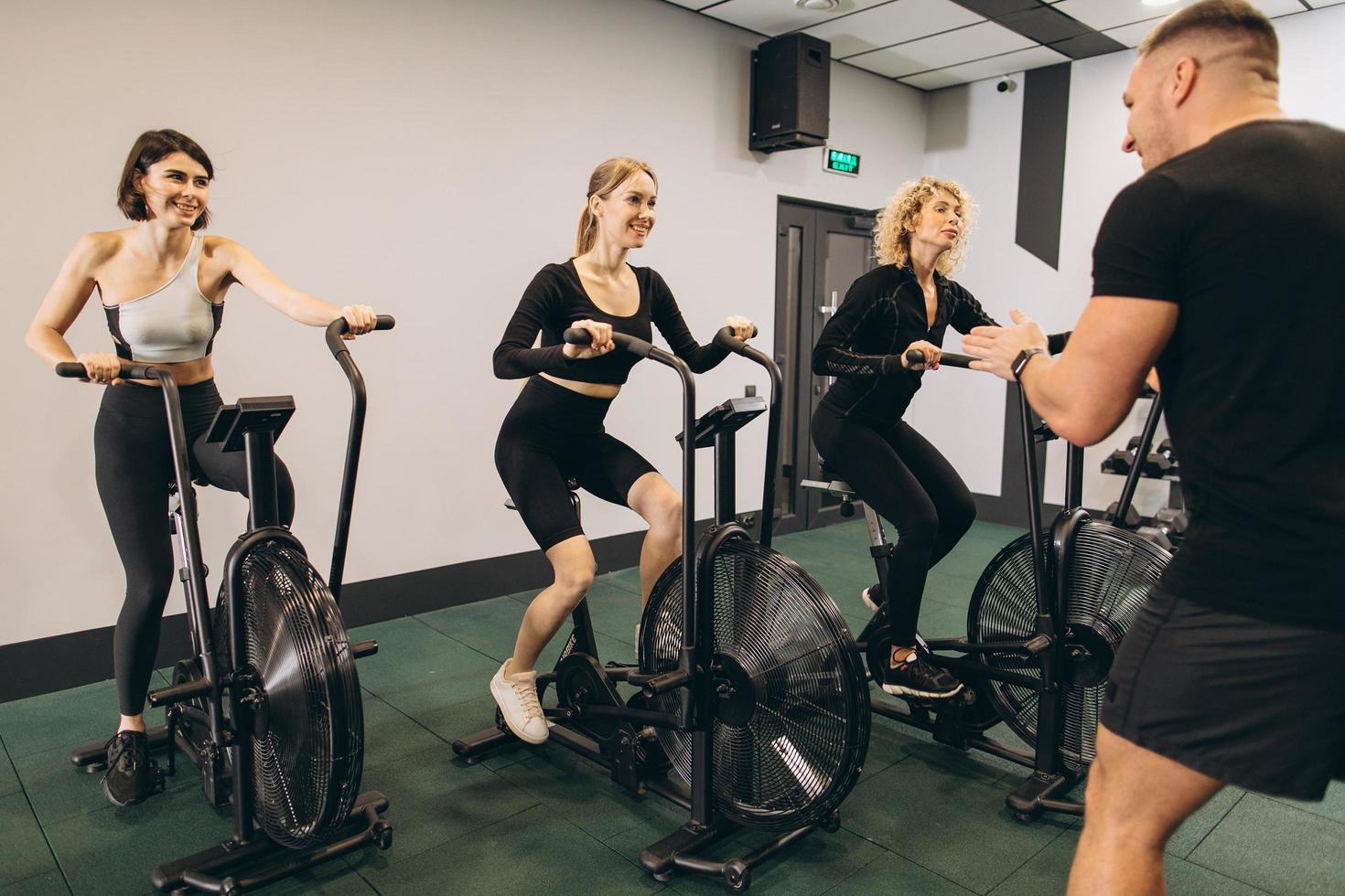 Young women make exercising on air bikes at gym with trainer motivating. photo