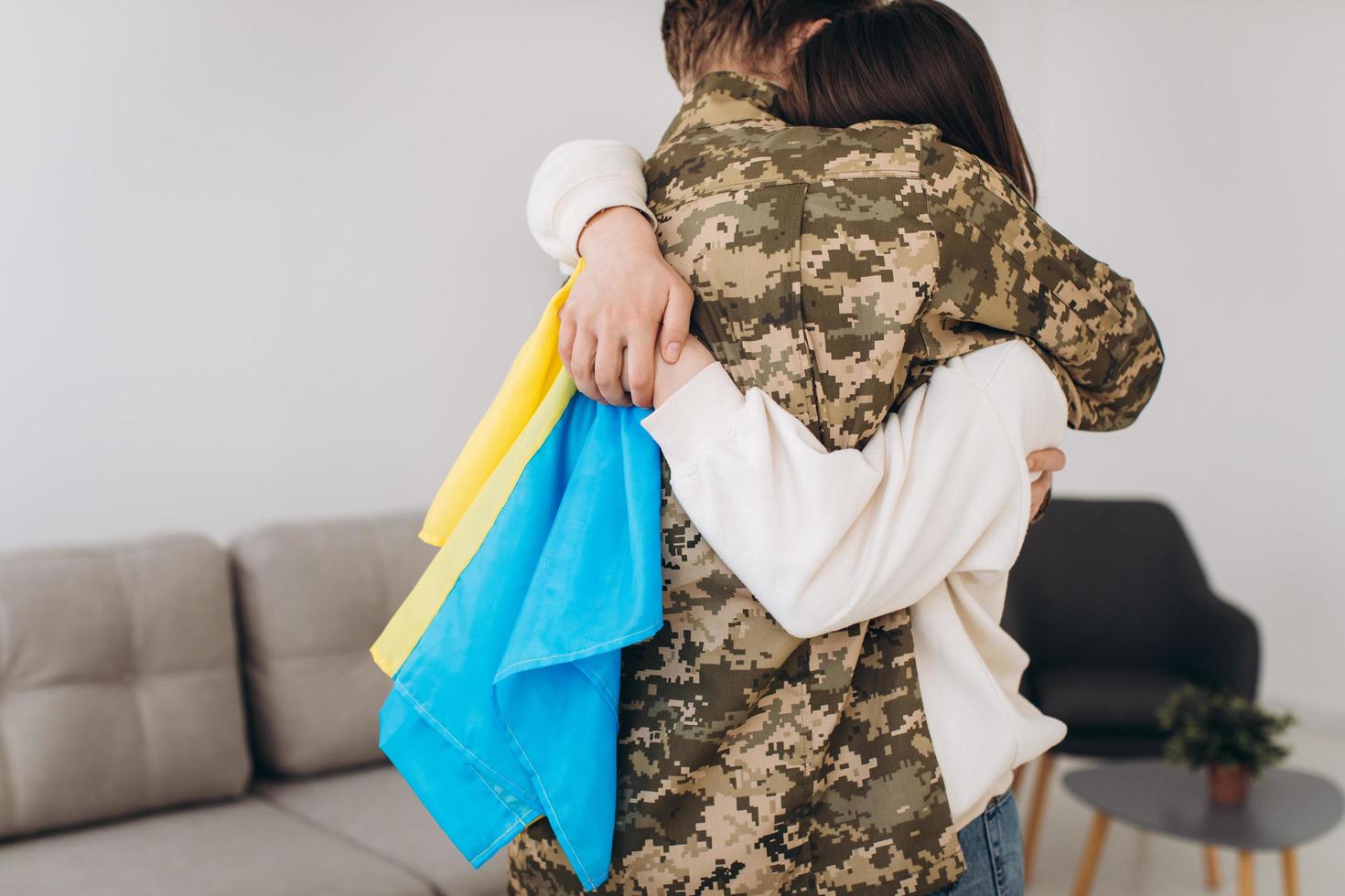 A Ukrainian girl hugs and holds a yellow and blue flag of a military man in uniform and says goodbye to him. photo