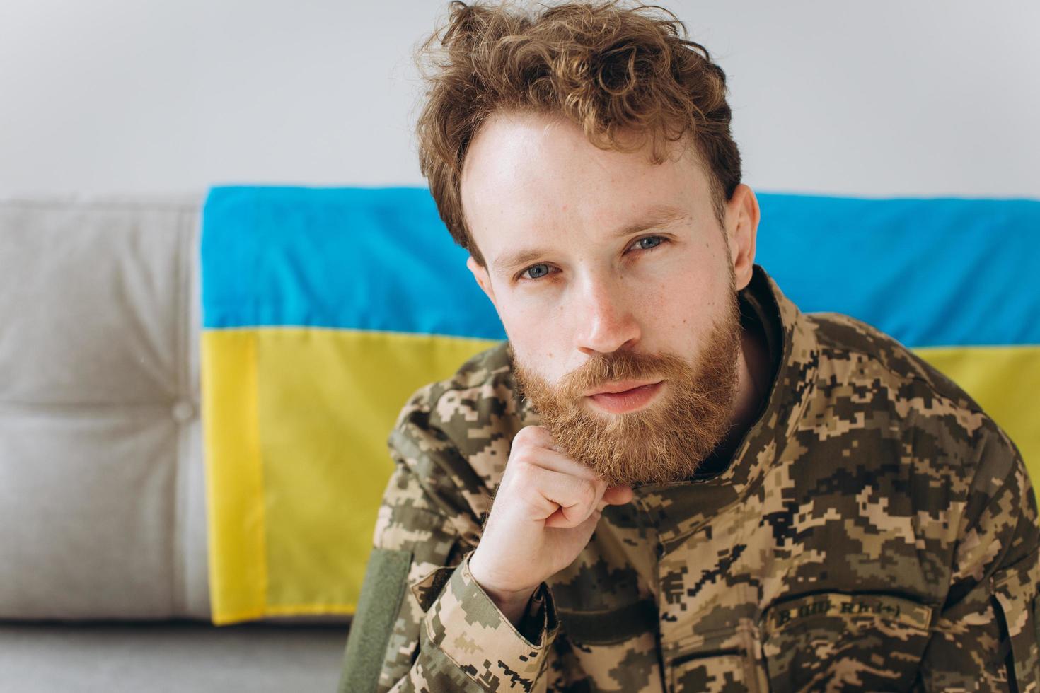 retrato de un emotivo joven soldado patriota ucraniano con uniforme militar sentado en la oficina en un sofá con una bandera amarilla y azul. foto