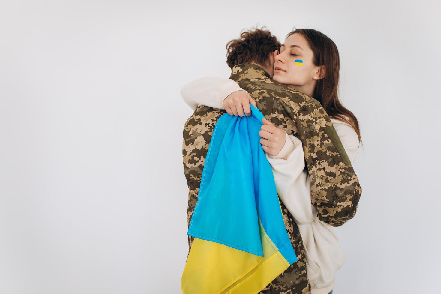 A Ukrainian girl hugs and holds a yellow and blue flag of a military man in uniform and says goodbye to him. photo