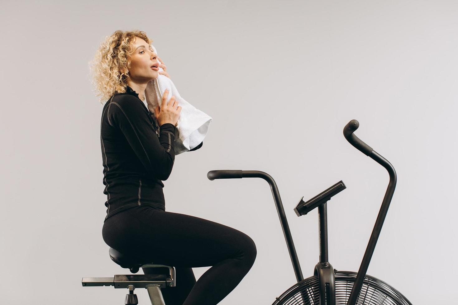 mujer crossfit haciendo entrenamiento cardiovascular intenso en bicicleta de aire. mujer limpiada con una toalla. foto