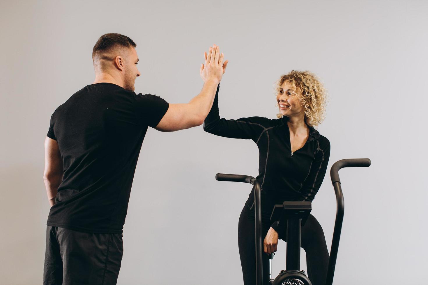 Young man and woman giving respect to each other and using air bike for cardio workout at cross training gym photo