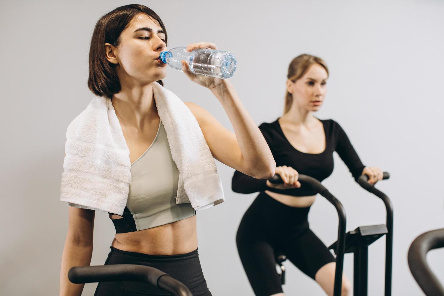 Young women drinking water and using air bike for cardio workout at cross training gym photo