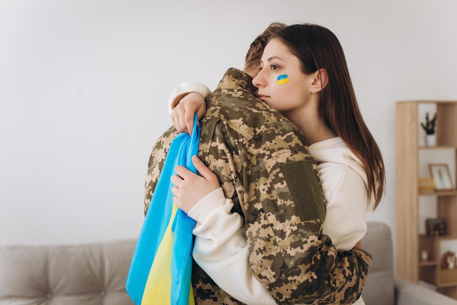 A Ukrainian girl hugs and holds a yellow and blue flag of a military man in uniform and says goodbye to him. photo