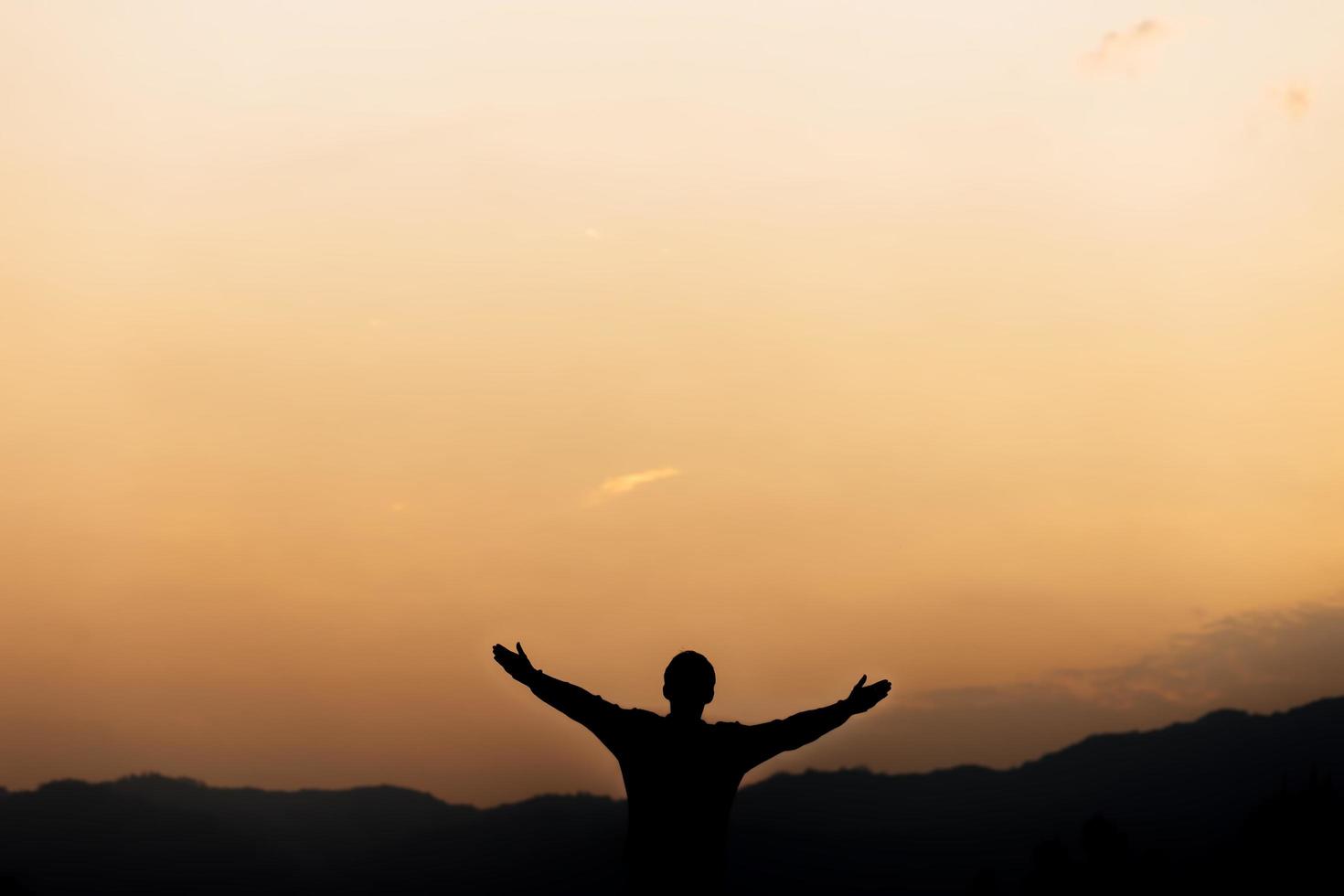 silueta de un hombre de pie levanta las manos y reza y adora a Dios al atardecer. concepto de religión. foto