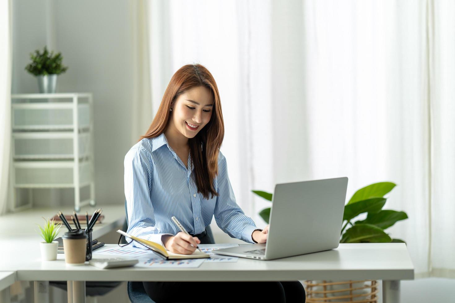 Beautiful young Asian girl working at a office space with a laptop. Concept of smart female business. photo