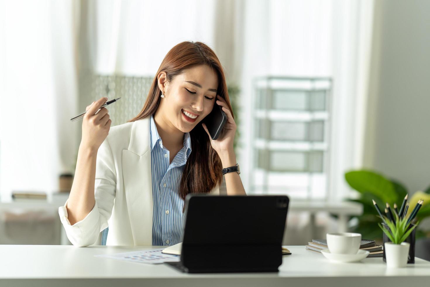 Young business woman on the phone at office. Business woman texting on the phone and working on laptop. Pretty young business woman sitting on workplace. Smiling business woman. photo