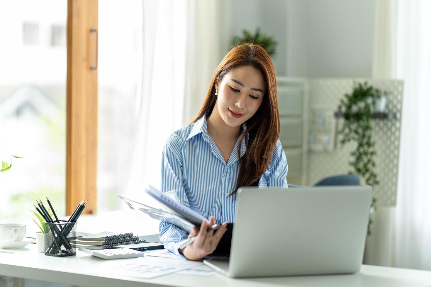 Young beautiful woman using her laptop while sitting in a chair at her working place. photo