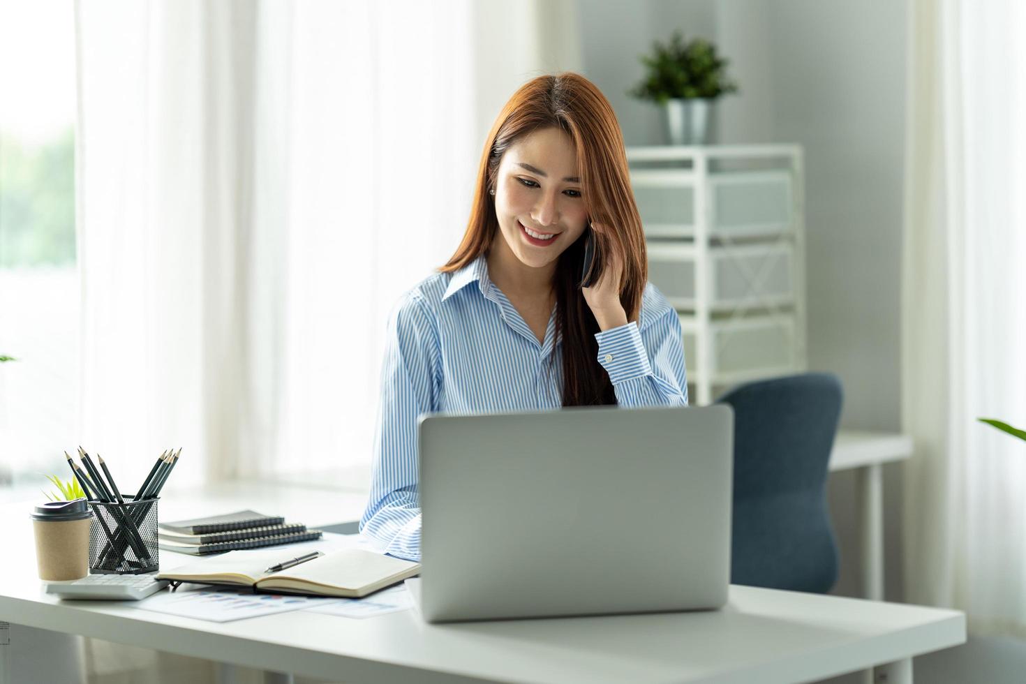 Asian businesswoman in formal suit in office happy and cheerful during using smartphone and working photo