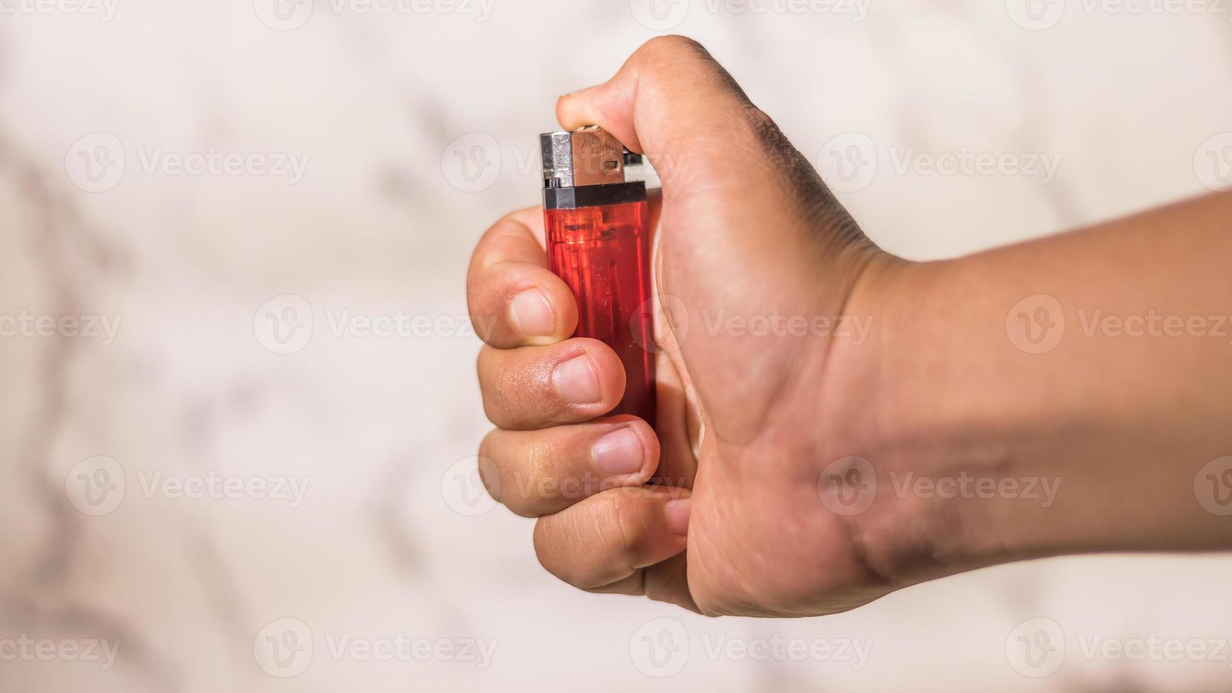 hand of man lighting cigarette lighter against bright background photo