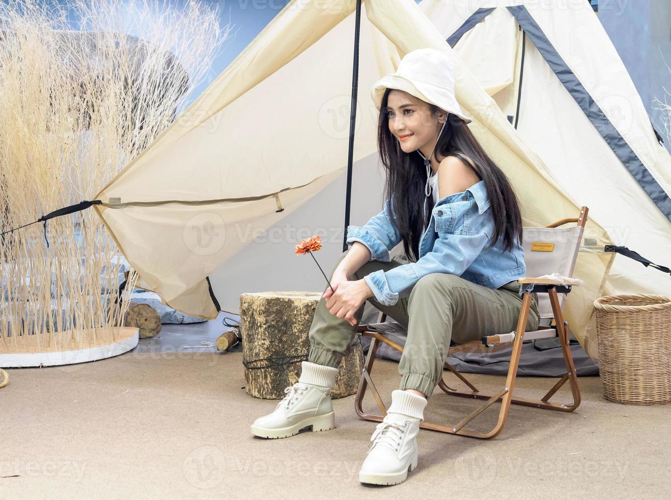 Portrait beautiful young girl woman Asian pretty smile one person alone sitting on chair camping with teble flower in vase lantern red travel trip in front tent freedom relax happy enjoy in vacation photo