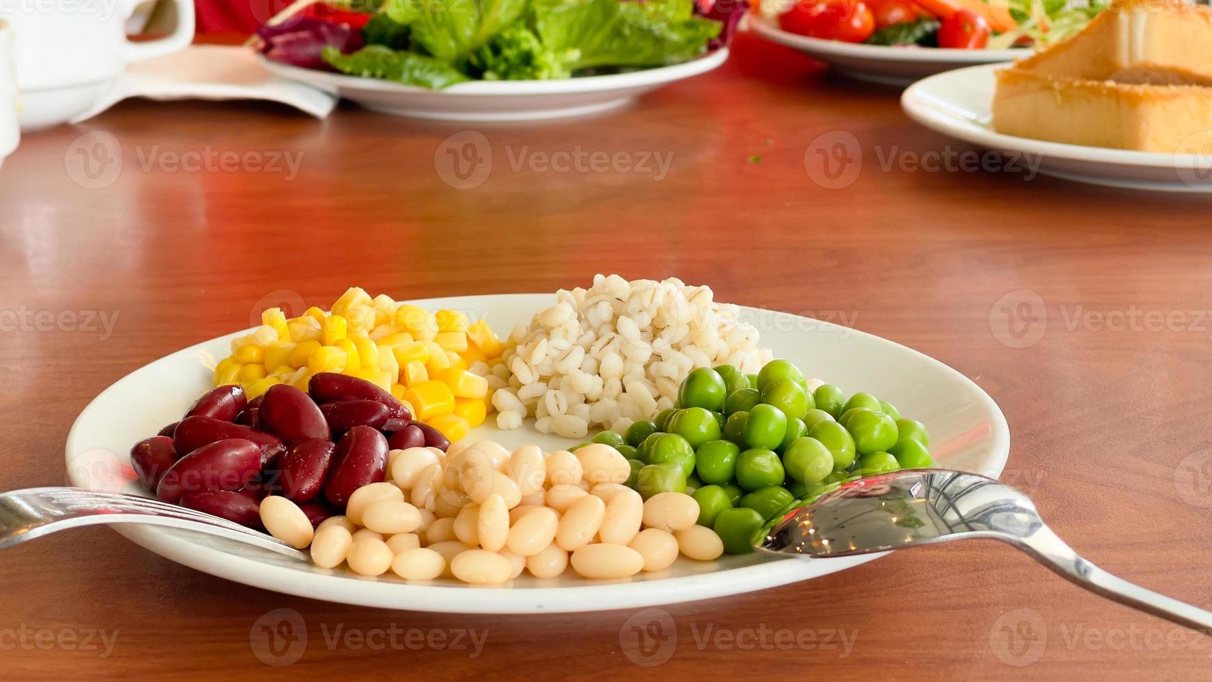 top view of navy bean and red bean and corn and  green peas and millet in white plate on wood background photo