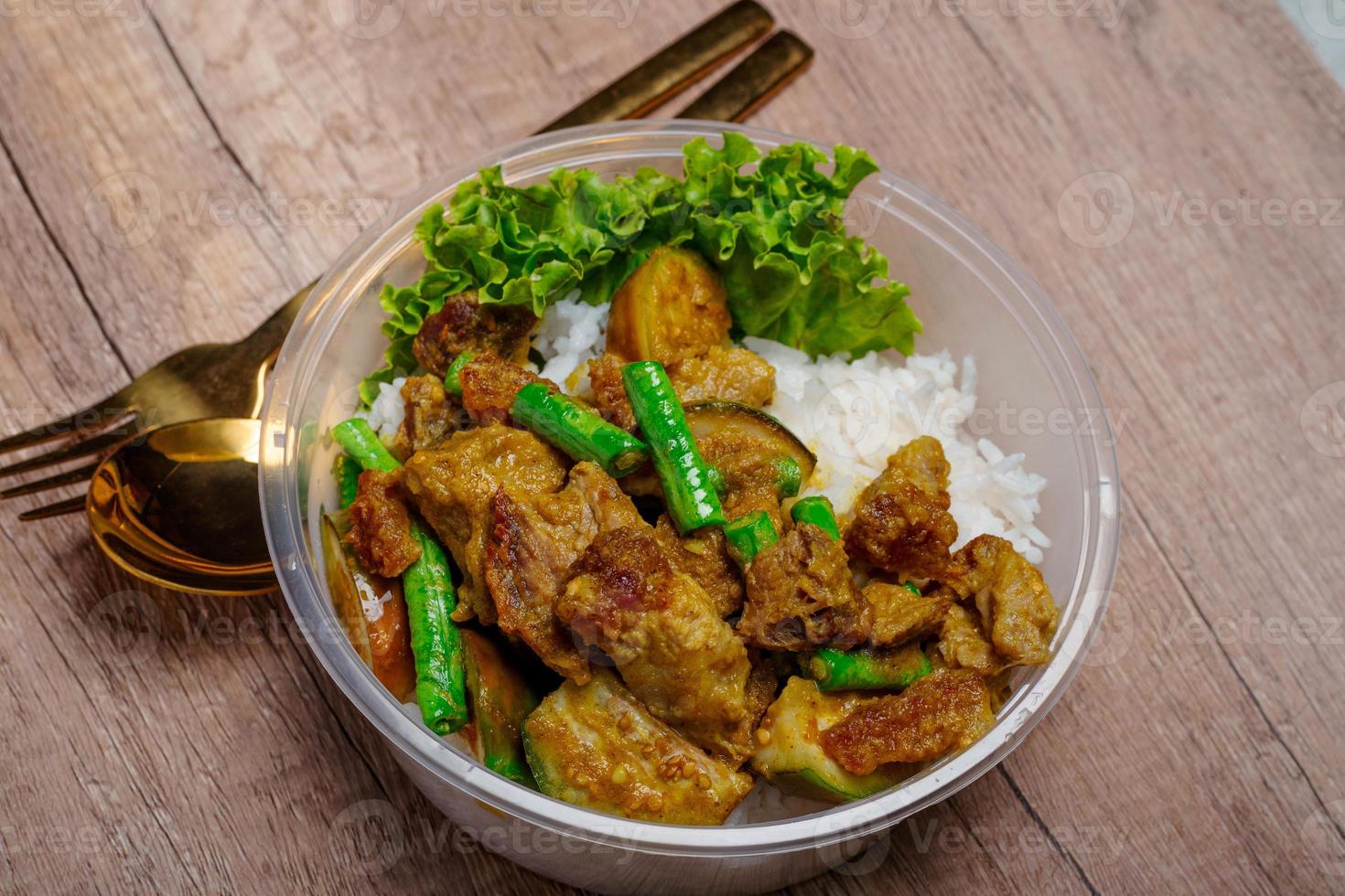 Fried crispy pork with green curry paste and vegetables in plastic cups on wooden floor photo