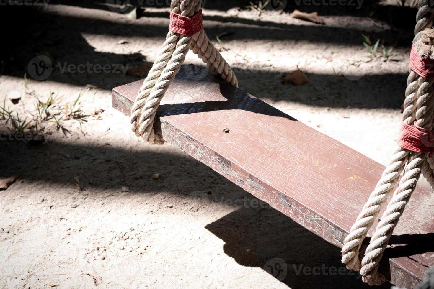 A wooden swing with twine tied to a tree photo