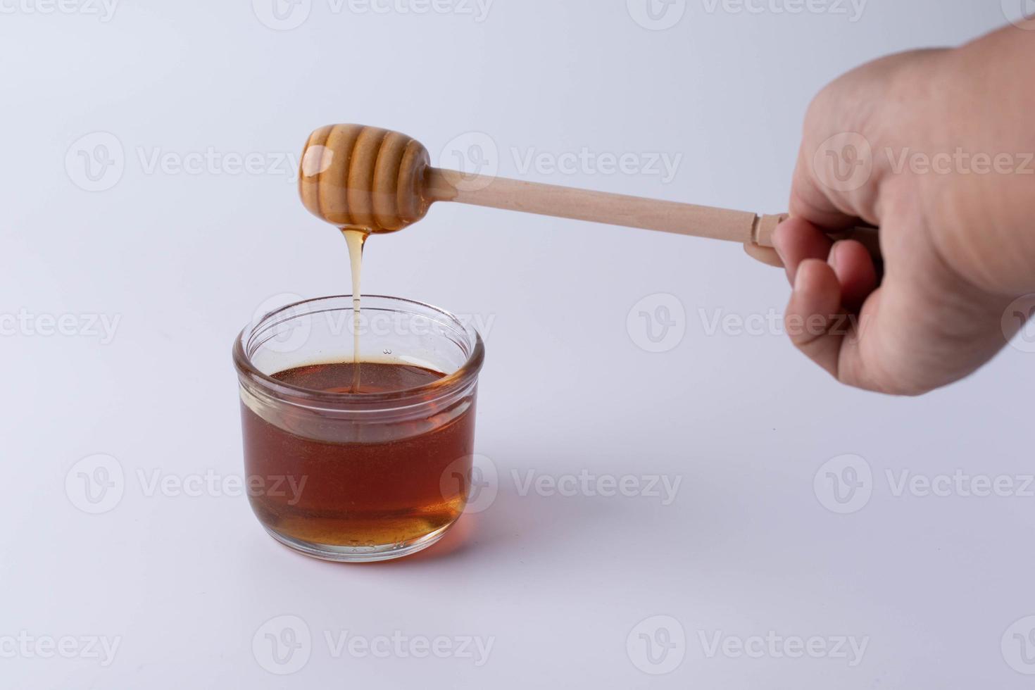 miel goteando del cucharón de miel en el frasco de vidrio transparente. foto