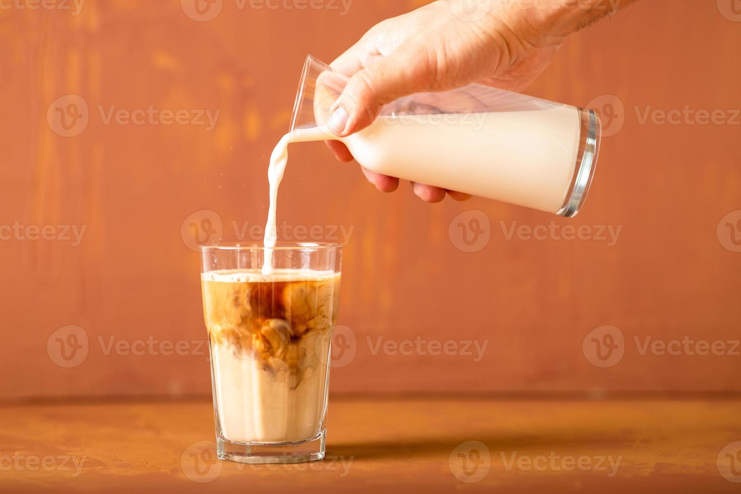 Hand is pouring milk to brewed coffee in studio with copy space. photo