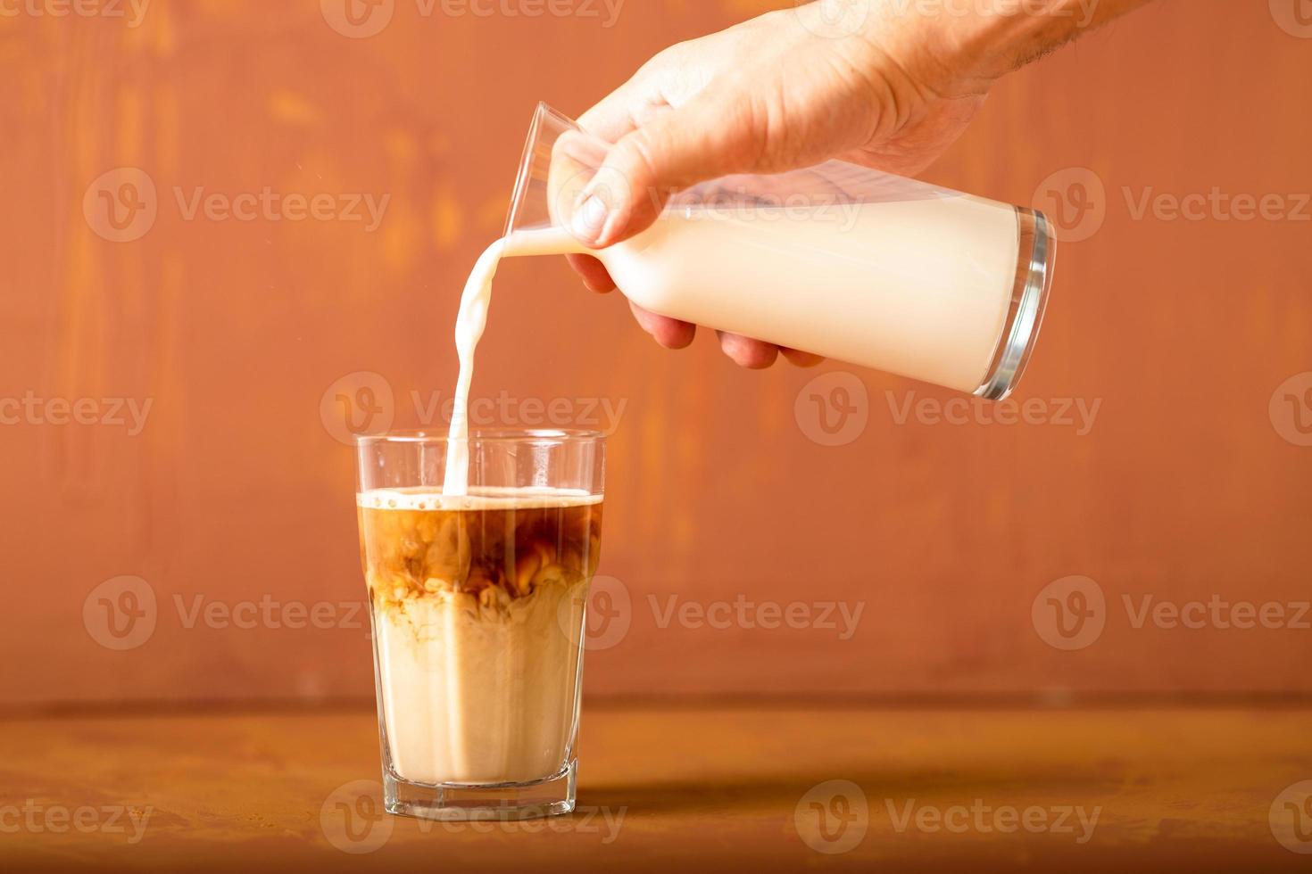 Hand is pouring milk to brewed coffee in studio with copy space. photo